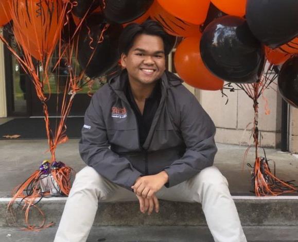 male student sitting on steps surrounded by orange and black balloons